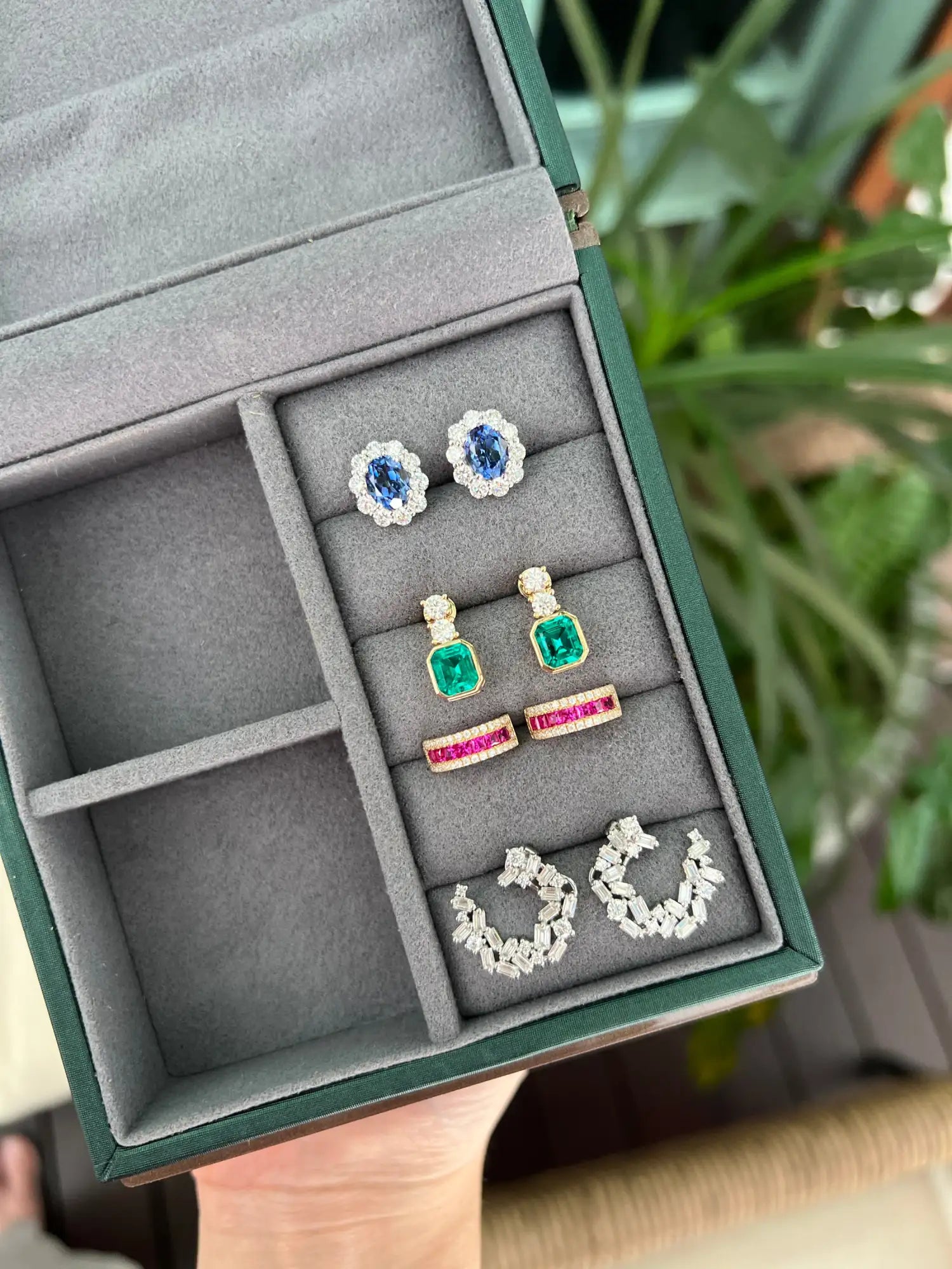 Green velvet jewelry box with multiple compartments and colorful earrings displayed inside.